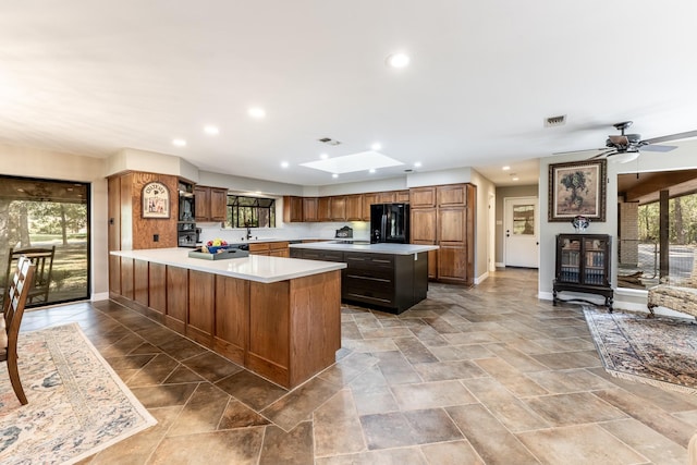 kitchen featuring a skylight, ceiling fan, kitchen peninsula, black refrigerator, and a kitchen island