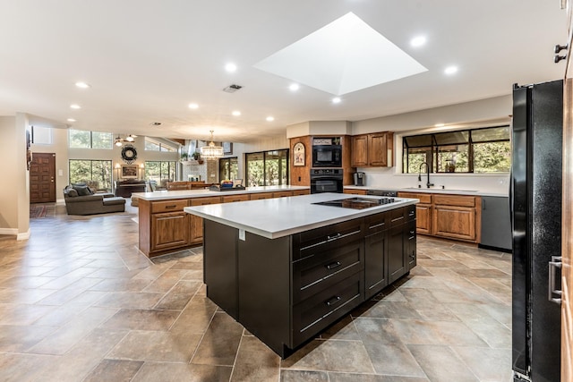 kitchen featuring a center island, black appliances, sink, a skylight, and a chandelier