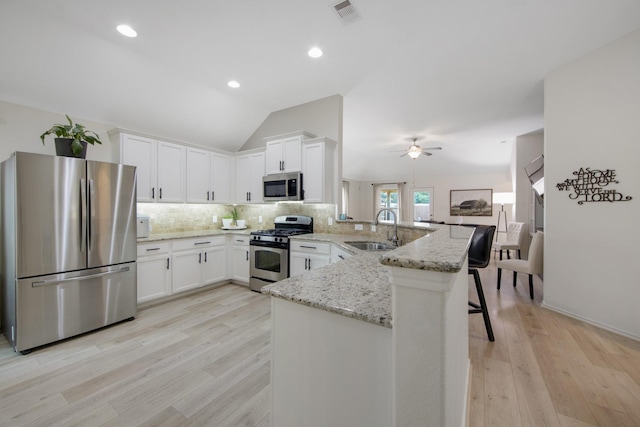 kitchen with kitchen peninsula, light wood-type flooring, stainless steel appliances, sink, and lofted ceiling