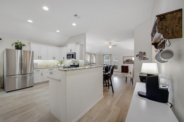 kitchen with white cabinets, light hardwood / wood-style flooring, vaulted ceiling, decorative backsplash, and appliances with stainless steel finishes