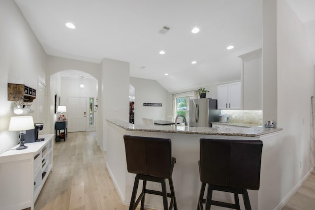 kitchen with kitchen peninsula, light stone countertops, vaulted ceiling, white cabinetry, and stainless steel refrigerator