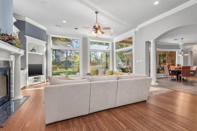 unfurnished living room featuring ceiling fan, built in shelves, ornamental molding, a fireplace, and light hardwood / wood-style floors