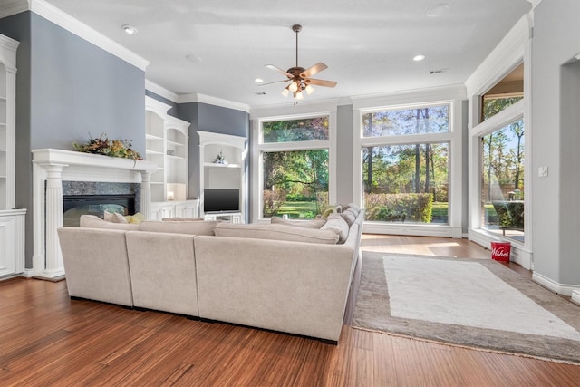 living room featuring ornamental molding, ceiling fan, built in features, a premium fireplace, and hardwood / wood-style floors