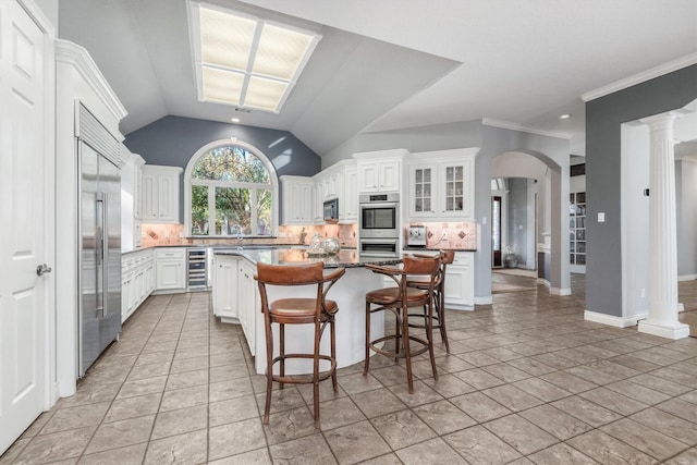 kitchen with decorative backsplash, decorative columns, stainless steel appliances, a center island, and white cabinetry