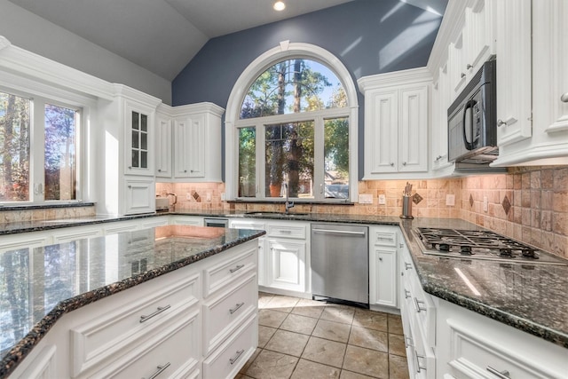 kitchen with dark stone counters, white cabinets, stainless steel appliances, and vaulted ceiling