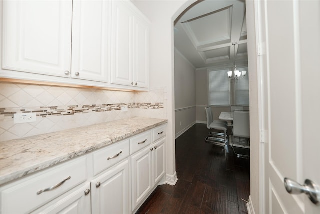 interior space with dark hardwood / wood-style flooring, light stone counters, coffered ceiling, white cabinets, and a chandelier