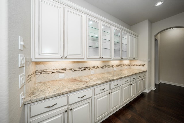 bar featuring light stone countertops, decorative backsplash, white cabinetry, and dark wood-type flooring