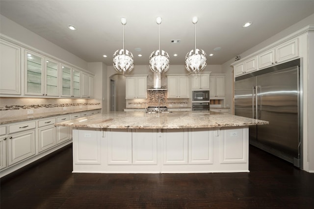 kitchen featuring a center island with sink, built in appliances, light stone countertops, tasteful backsplash, and decorative light fixtures