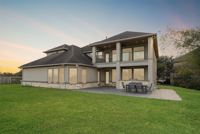 back house at dusk with a yard, a patio area, ceiling fan, and a balcony