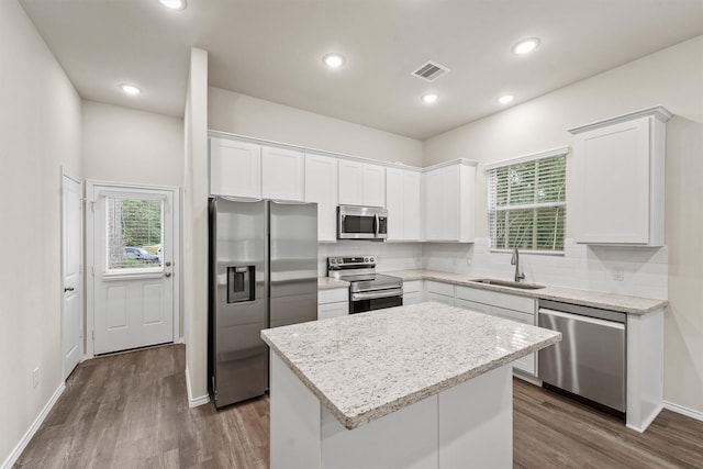 kitchen featuring light stone countertops, appliances with stainless steel finishes, sink, a center island, and white cabinetry