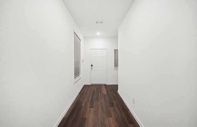 hallway with dark wood finished floors, visible vents, and baseboards