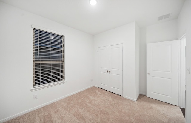 unfurnished bedroom featuring light carpet, visible vents, a closet, and baseboards