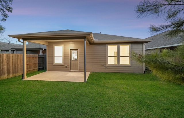 back of house at dusk featuring a yard, a patio, and fence