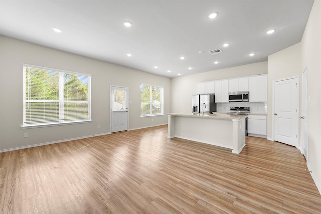 kitchen with white cabinets, stainless steel appliances, light hardwood / wood-style floors, and an island with sink