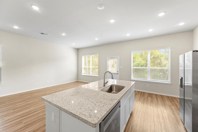 kitchen featuring appliances with stainless steel finishes, light wood-type flooring, sink, a center island with sink, and white cabinetry