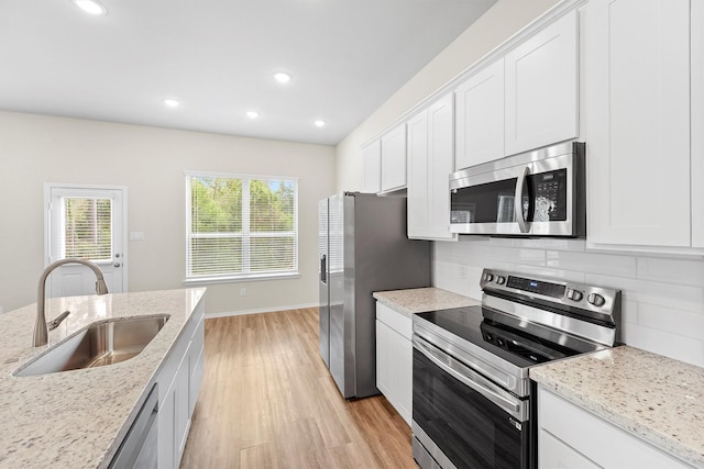 kitchen featuring appliances with stainless steel finishes, light wood-type flooring, light stone counters, sink, and white cabinets