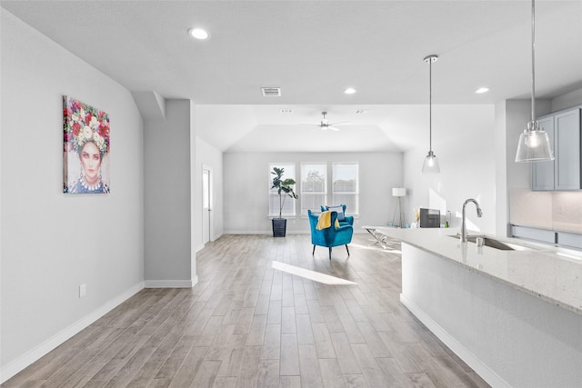 kitchen with light stone countertops, ceiling fan, sink, decorative light fixtures, and light hardwood / wood-style flooring