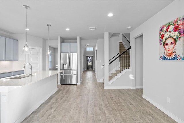 kitchen with stainless steel fridge, light wood-type flooring, decorative light fixtures, and an island with sink