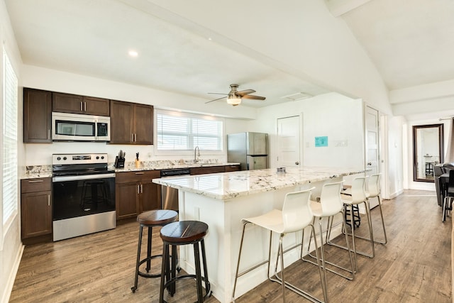 kitchen with wood-type flooring, appliances with stainless steel finishes, a center island, and a breakfast bar