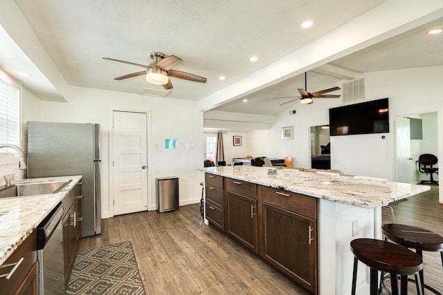 kitchen featuring a kitchen bar, sink, vaulted ceiling with beams, appliances with stainless steel finishes, and dark hardwood / wood-style flooring