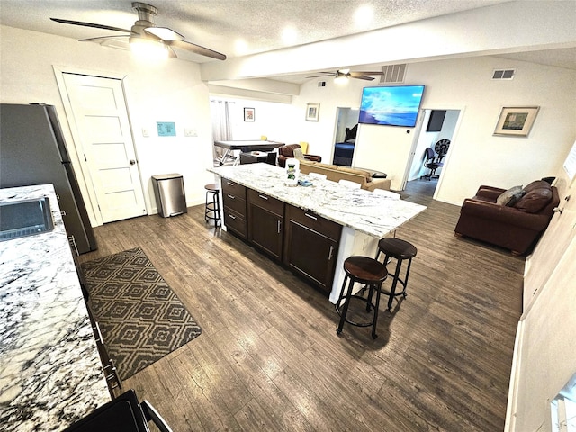 kitchen with dark hardwood / wood-style floors, a kitchen breakfast bar, a center island, dark brown cabinetry, and light stone counters