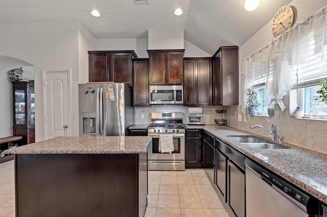 kitchen featuring a center island, sink, light stone countertops, a textured ceiling, and appliances with stainless steel finishes