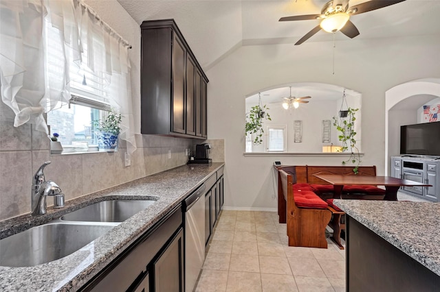 kitchen with dishwasher, sink, light tile patterned floors, dark brown cabinets, and light stone counters