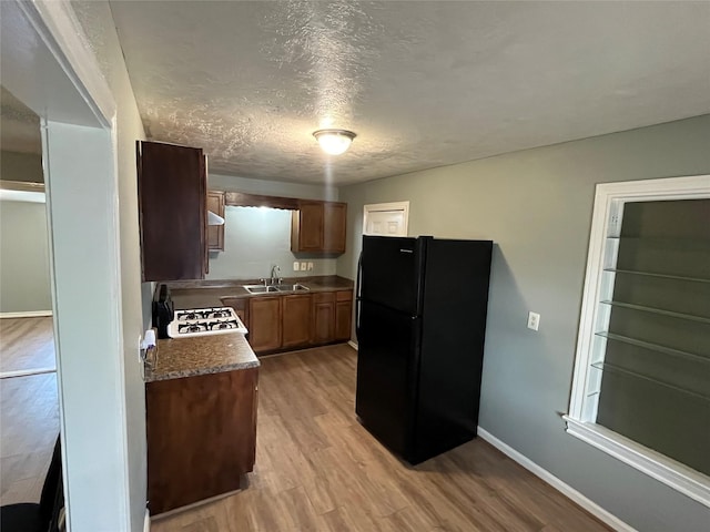 kitchen featuring light wood-type flooring, black fridge, white gas stove, and sink