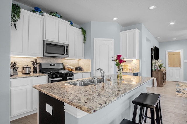 kitchen featuring sink, stainless steel appliances, white cabinetry, and an island with sink