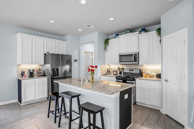 kitchen featuring white cabinets, sink, an island with sink, tasteful backsplash, and stainless steel appliances