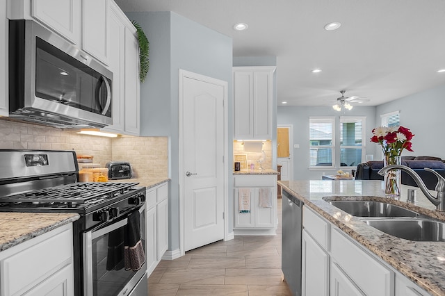 kitchen with sink, ceiling fan, light stone counters, white cabinetry, and stainless steel appliances