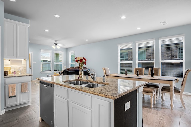 kitchen featuring stainless steel dishwasher, white cabinets, sink, and an island with sink