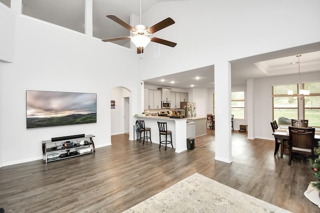 living room featuring ceiling fan with notable chandelier, dark wood-type flooring, high vaulted ceiling, and a tray ceiling