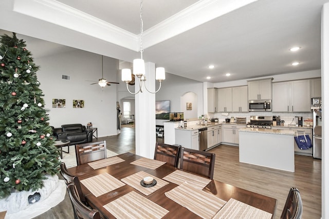 dining area with a tray ceiling, hardwood / wood-style floors, ceiling fan with notable chandelier, and ornamental molding