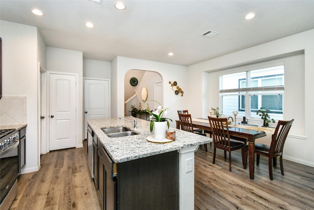 kitchen with arched walkways, stainless steel range, visible vents, a sink, and an island with sink