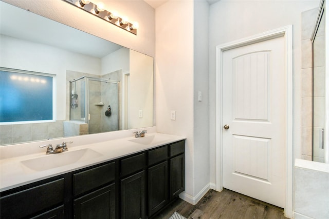 full bath with double vanity, a stall shower, a sink, and wood finished floors