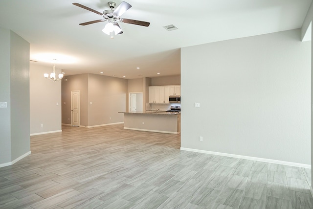 unfurnished living room featuring ceiling fan with notable chandelier and light hardwood / wood-style floors