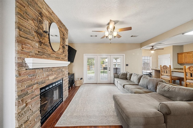 living room with ceiling fan, french doors, dark hardwood / wood-style flooring, a textured ceiling, and a fireplace