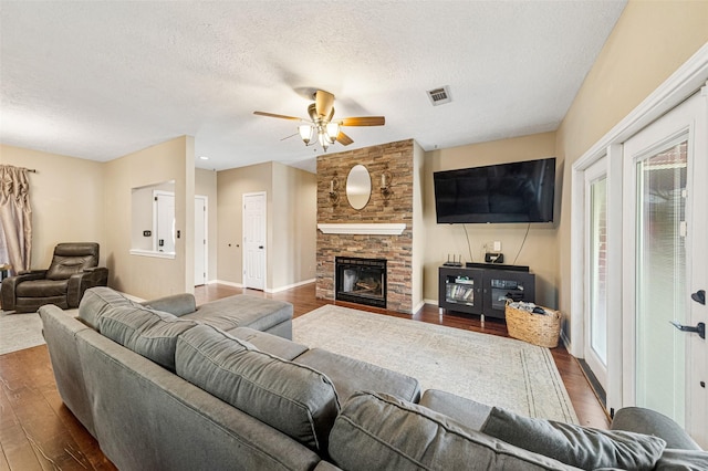 living room with ceiling fan, a fireplace, dark wood-type flooring, and a textured ceiling