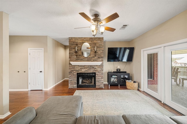 living room featuring hardwood / wood-style floors, a textured ceiling, a stone fireplace, and ceiling fan