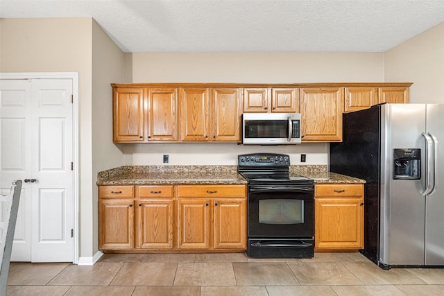 kitchen with dark stone countertops, light tile patterned floors, a textured ceiling, and appliances with stainless steel finishes