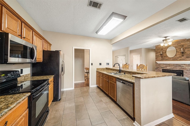 kitchen featuring appliances with stainless steel finishes, a brick fireplace, a textured ceiling, sink, and light tile patterned flooring