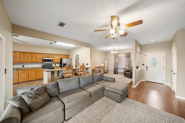 living room with ceiling fan with notable chandelier, light wood-type flooring, and a textured ceiling