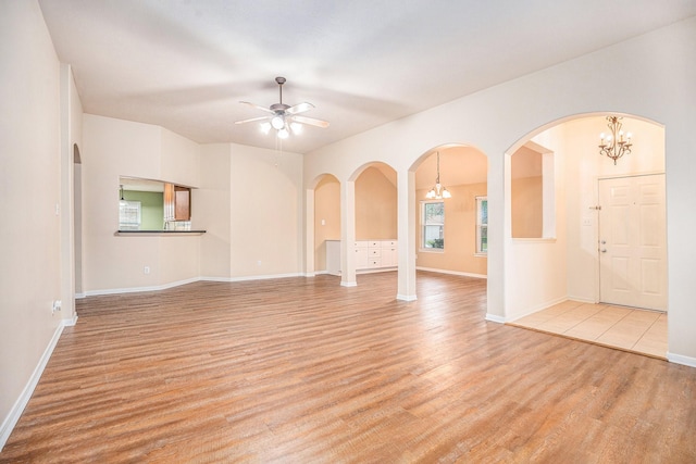 spare room with light wood-style flooring, arched walkways, baseboards, and ceiling fan with notable chandelier