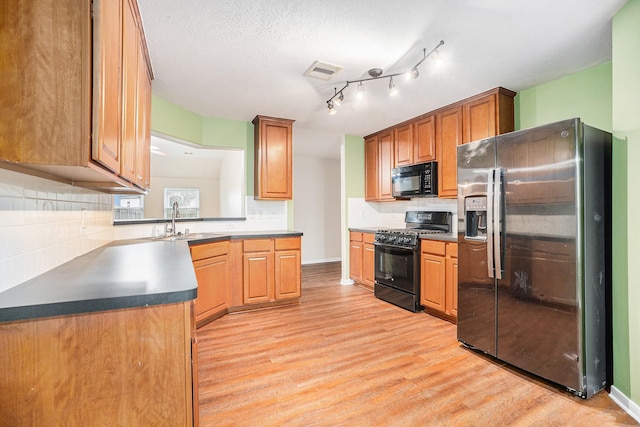 kitchen with a sink, visible vents, light wood-type flooring, backsplash, and black appliances