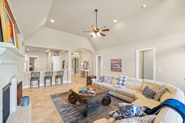 tiled living room with high vaulted ceiling, ceiling fan with notable chandelier, and a tile fireplace