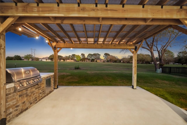 patio terrace at dusk with exterior kitchen, a pergola, a yard, and grilling area