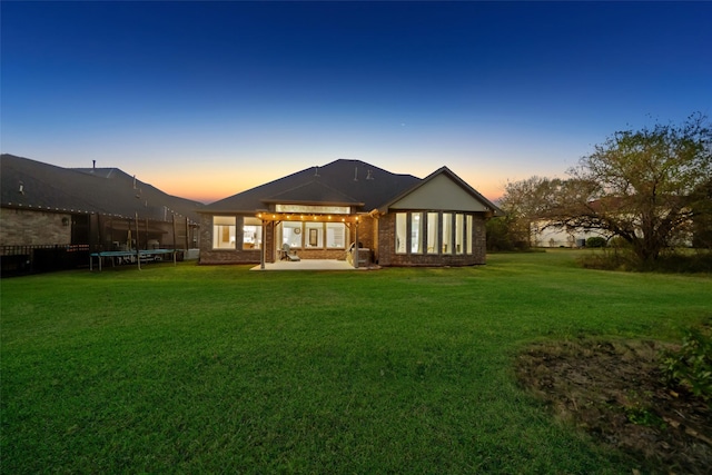 back house at dusk with a patio area, a trampoline, and a lawn