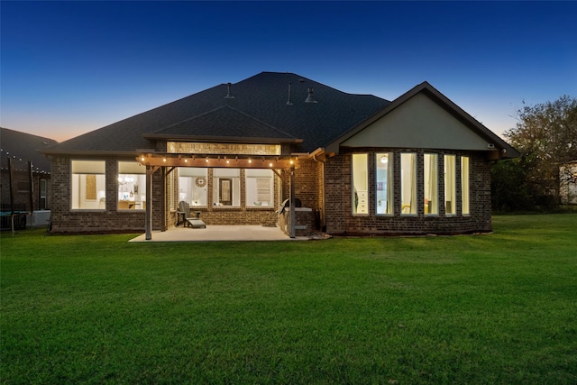 back house at dusk with a yard, a patio area, and a trampoline