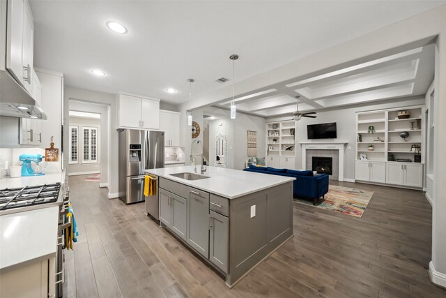 kitchen with stainless steel appliances, hanging light fixtures, a fireplace, white cabinets, and a center island with sink